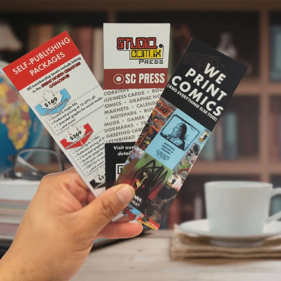 Three SC Press bookmarks fanned in one hand, one reading 'We print comics (and everything else too)'
