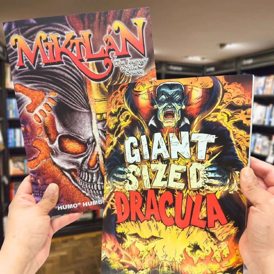 Two graphic novels held up in a bookshop, Miktán and Giant Sized Dracula